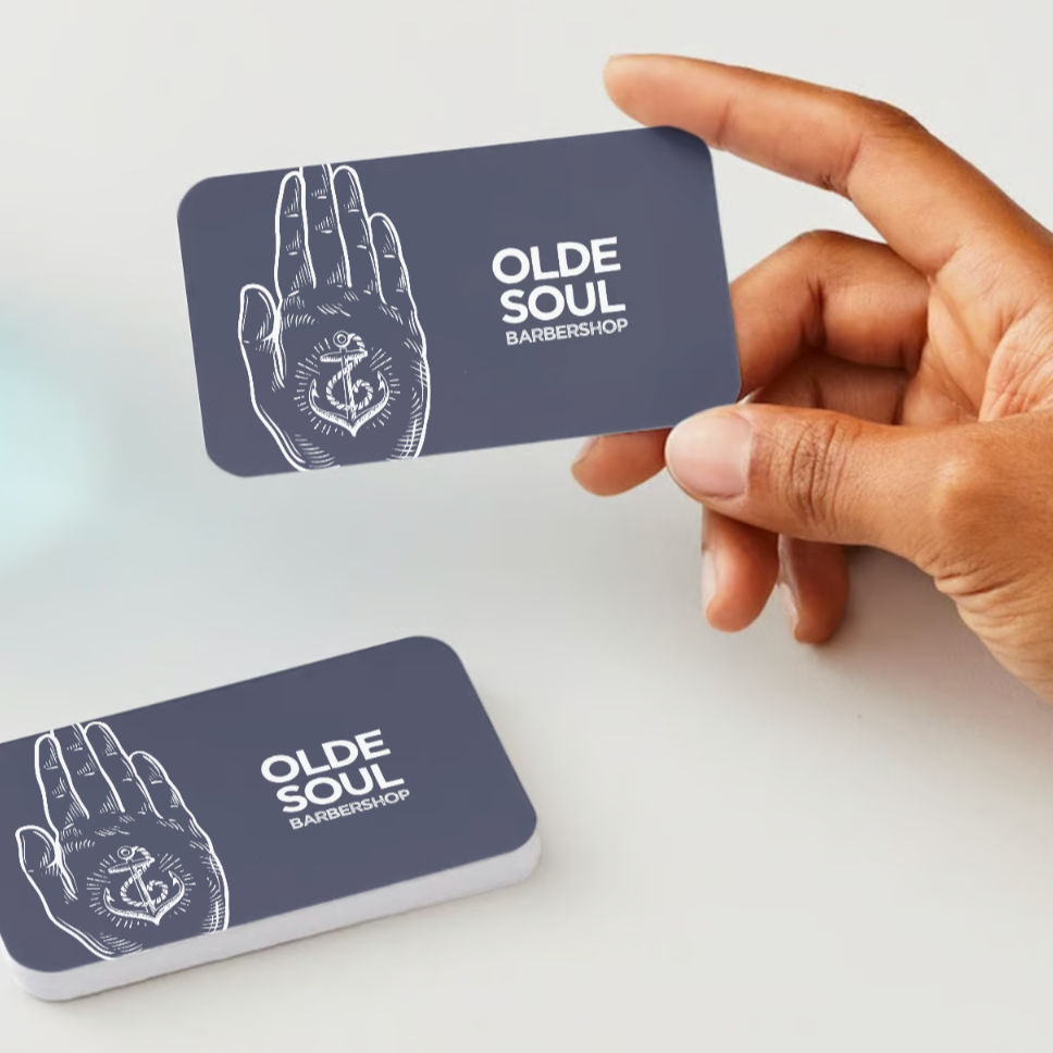 Photo of hand holding olde soul barbershop gift card with a stack of gift cards on the table
